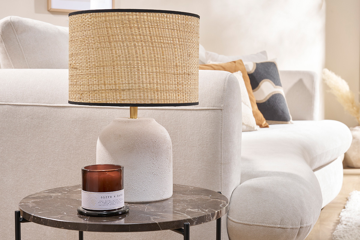 Lampe � poser en c�ramique blanche et raphia sur table en marbre, canap� beige en arri�re-plan.