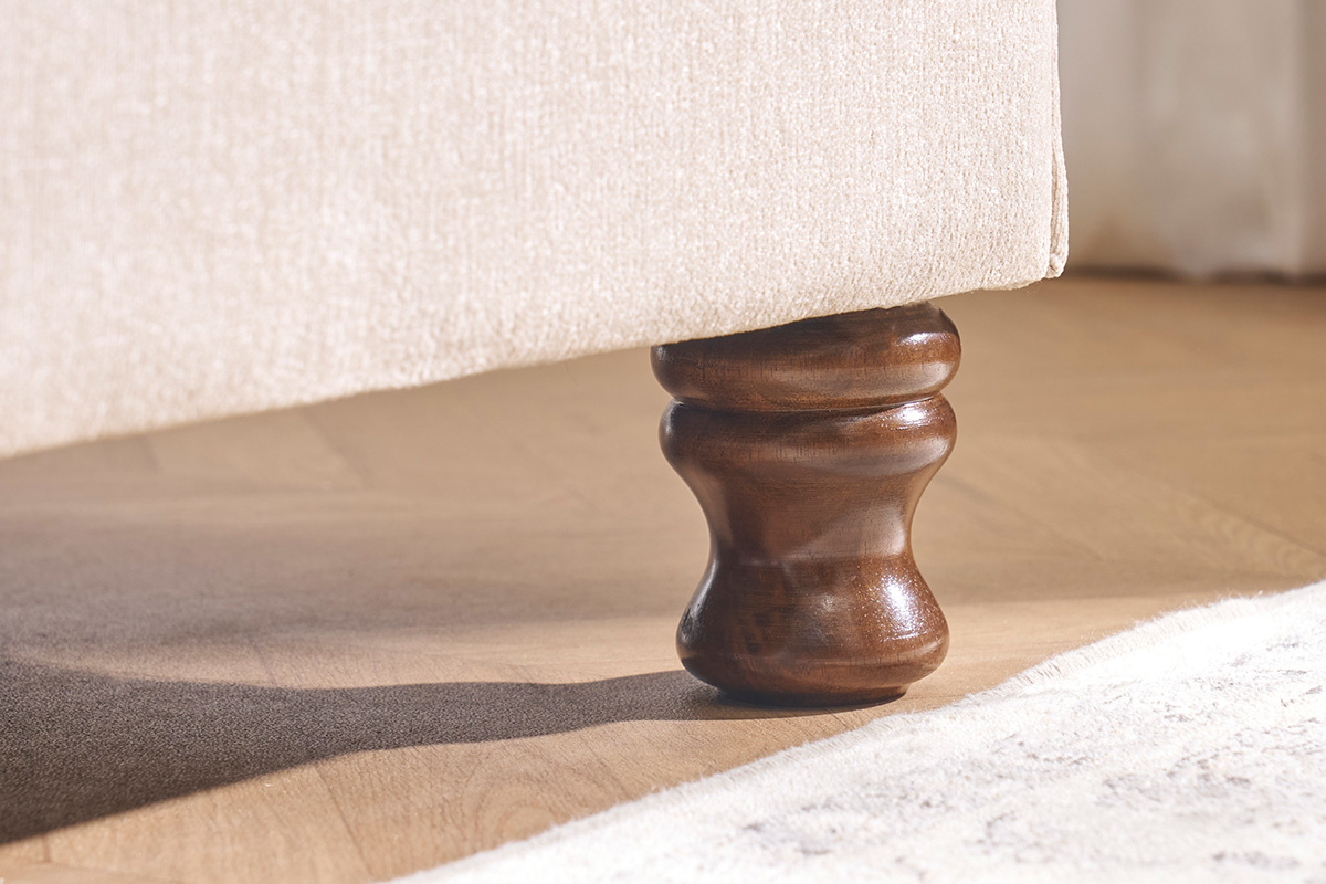 Pied en bois sculpt� d'un lit 2 places en velours beige, vue en gros plan.